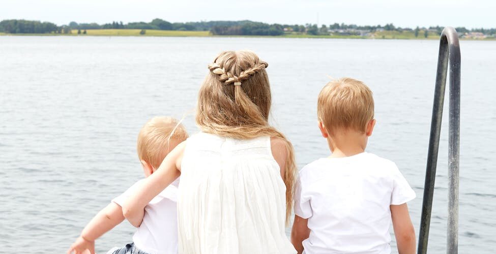 woman wearing white halter dress beside kid wearing white crew neck shirt near body of water